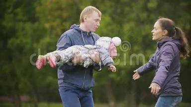 快乐的家庭：爸爸、妈妈和小女孩在秋天的公园散步：妈妈拥抱爸爸和宝宝，慢动作
